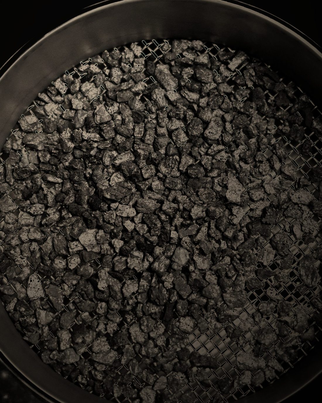 Activated carbon granules resting on a stainless-steel test sieve during particle-size analysis